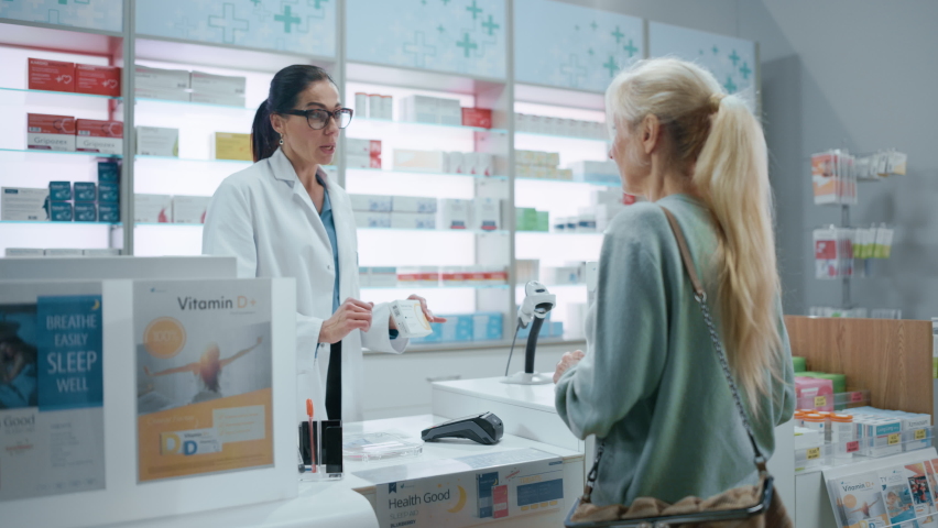 Pharmacy Drugstore Checkout Cashier Counter: Female Pharmacist Explains Use and Manual for Prescription Medicine Beautiful Senior Female Customer Paying Using Contactless Credit Card to Terminal Royalty-Free Stock Footage #1066836154
