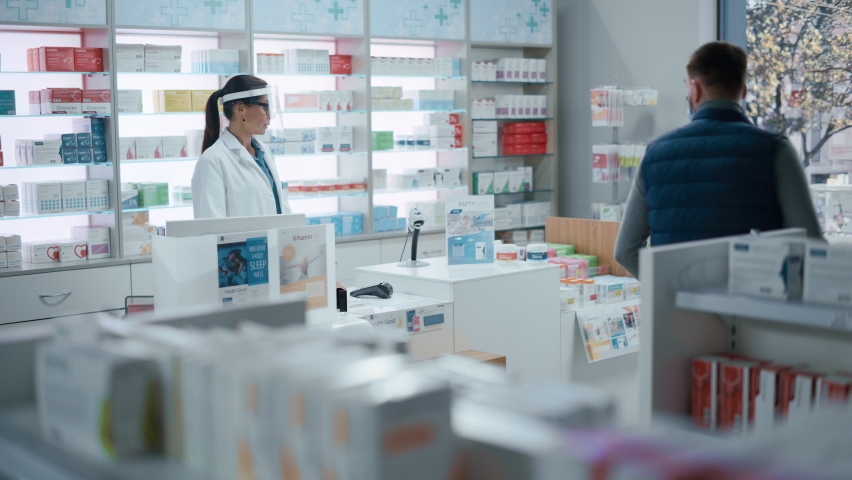 Pharmacy Drugstore Checkout Counter: Female Pharmacist Wearing Face Shields Selling Medicine Package, Customer with Face Mask Using NFC Smartphone with Contactless Payment Terminal and Credit Card | Shutterstock HD Video #1066836172