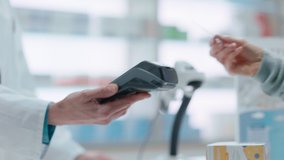 Pharmacy Drugstore Checkout Cashier Counter: Pharmacist and a Customer Using Contactless Credit Card with Payment Terminal to Buy Prescription Medicine, Health Care Goods. Close-up Focus on Hands - Powered by Shutterstock - Get 15% off with code: PIKWIZARD15