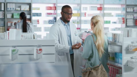 Pharmacy: Professional Black Male Pharmacist Helping Beautiful Senior Female Customer with Medicine Recommendation, Advice, Talking. Drugstore with Full of Drugs, Pills, Health Care, Beauty Products