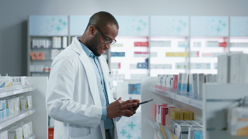 Pharmacy: Portrait of Professional Black Pharmacist Uses Digital Tablet Computer, Checks Inventory of Medicine, Looks at Camera and Smiles Charmingly. Drugstore Store With Health Care Products Royalty-Free Stock Footage #1066836322