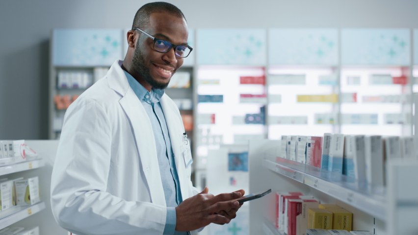 Pharmacy: Portrait of Professional Black Pharmacist Uses Digital Tablet Computer, Checks Inventory of Medicine, Looks at Camera and Smiles Charmingly. Drugstore Store With Health Care Products | Shutterstock HD Video #1066836322