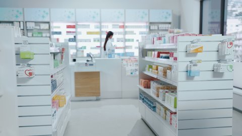 Modern Pharmacy Drugstore with Shelves full of Packages Full of Modern Medicine, Drugs, Vitamin Boxes, Supplements. In Background Professional Pharmacist Working at Checkout Counter. Static Shot