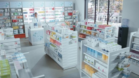 Modern Pharmacy Drugstore with Shelves full of Packages Full of Modern Medicine, Drugs, Vitamin Boxes, Supplements. In Background Anonymous Customer Buys Products from Pharmacist Standing at Counter
