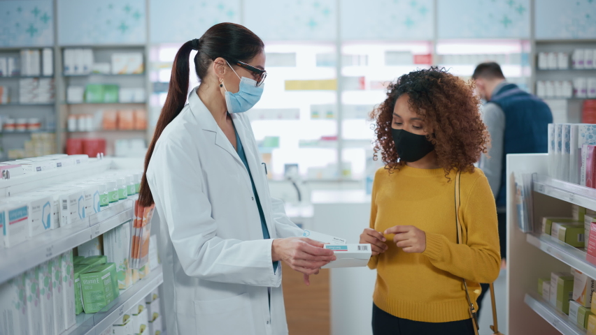 Covid-19 Pharmacy Wearing Face Masks: Professional Pharmacist Helping Beautiful Female Customer with Medicine Recommendation, Talking. Drugstore with Full of Drugs, Pills, Health Care, Beauty Products Royalty-Free Stock Footage #1066836619