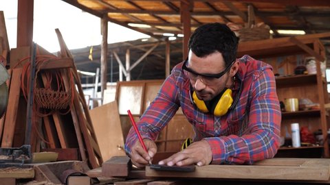 Carpenter wears protective leather gloves, with a pencil and the carpenter's square trace the cutting line on a wooden table. For DIY and factory concept.