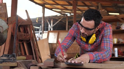 Carpenter wears protective leather gloves, with a pencil and the carpenter's square trace the cutting line on a wooden table. For DIY and factory concept.