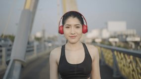Slow-motion video portrait. A white Asian woman wearing a black sports bra. Black trousers And red Headphones talking, looking at the camera
