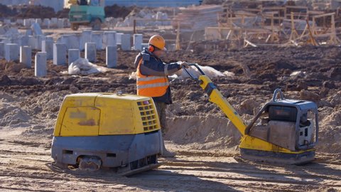 Two industrial, of yellow color, soil rammers compact the sand cushion for the road, one is remote-controlled and the one at the edge is directly controlled by the builder