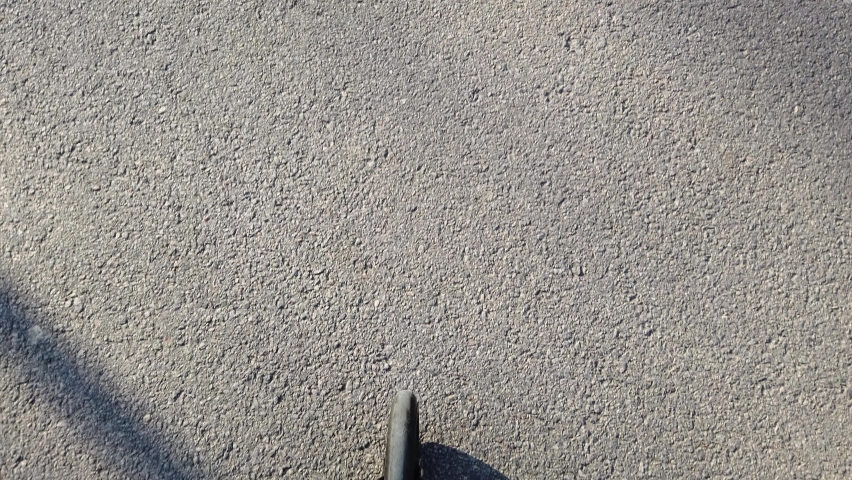 Riding an electric scooter on a sunny day - the view of wheel rolling on the asphalt road, in the first person