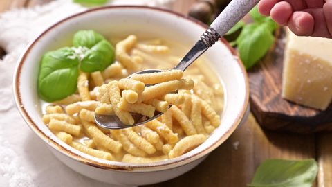 Passatelli in broth - pasta cooked in chicken broth. Hand takes the pasta with a spoon. A pasta formed of bread crumbs, eggs, grated Parmesan cheese. Typical for Pesaro, Urbino and Emilia Romagna. 