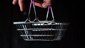 Hand holds a shopping basket on a black background. Delivery, ordering of goods concept.