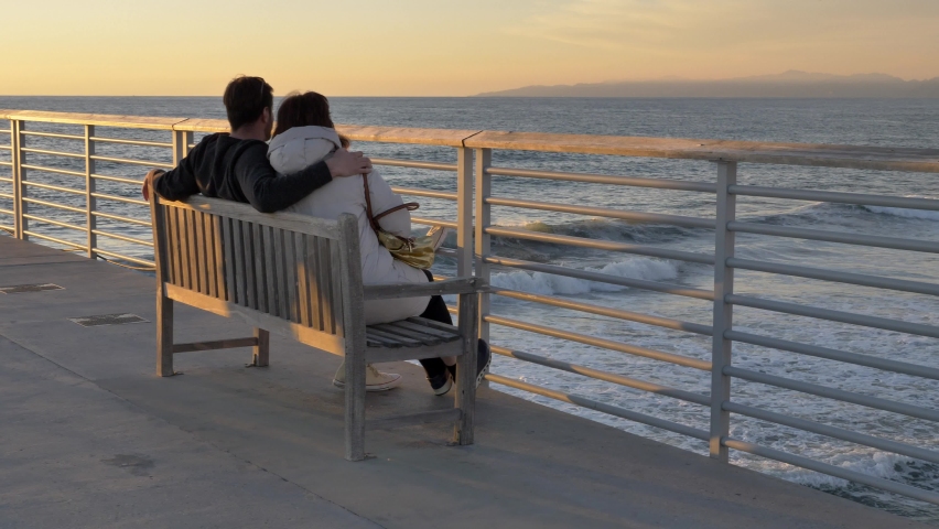 Couple men and woman at Hermosa Beach Pier famous La La Land scenary, enjoing beautiful view of ocean with sun flare