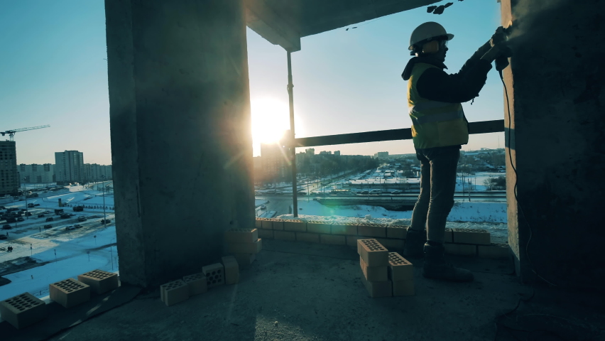 Male worker is buffing a wall of a multistory building in progress. A construction worker at a construction site.