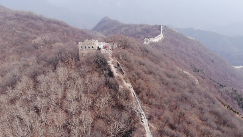 Watchtower and decay stone construction of Great Wall of China, aerial shot. Bare bushes on mountain slopes, early spring season view of Mutianyu section. Small tent seen near top-located tower