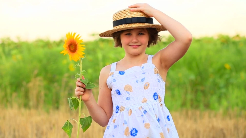 Adorable happy girl in hat holding sunflower and laugh on summer field. Beautiful cheerful teenage girl posing between yellow sunflowers in countryside