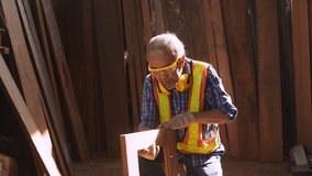 Video Slow motion of Asian elderly carpenter craftsman in carpentry shop being repaired and polished wooden window frame with sandpaper  to be tidy and beautiful and then blow away the dust.