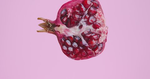 Juice flows down on natural pomegranate fruit on pink studio background with copy space, healthy eating concept