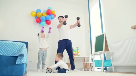 Young cheerful father is engaged in physical exercises with two sons. Dad with kids workout dumbbells at home in the room. Education, boys. Fun Daddy spends time with the children. Happy fathers day