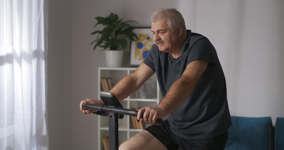 portrait of middle-aged person training on exercise bike at home, keeping fit and losing weight, cardio workout