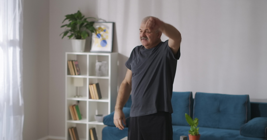 adult man is training at home at morning, raising hands alternately, healthy lifestyle at middle age