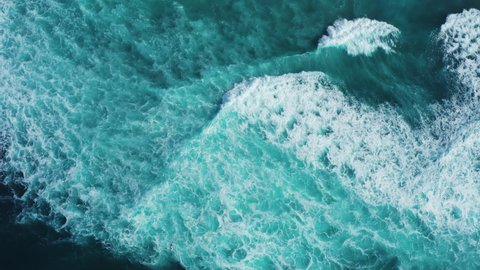 Aerial drone view of oceanic tidal waves rolling and creating foam patterns.