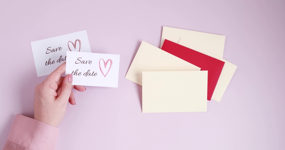 Woman hands putting save the date card in beige envelope. Wedding planning, invitation concept. Top view