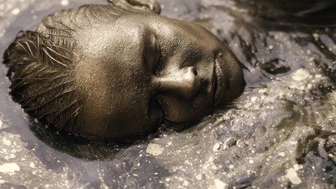 golden woman is lying in bath with shiny water, closeup of face with closed eyes