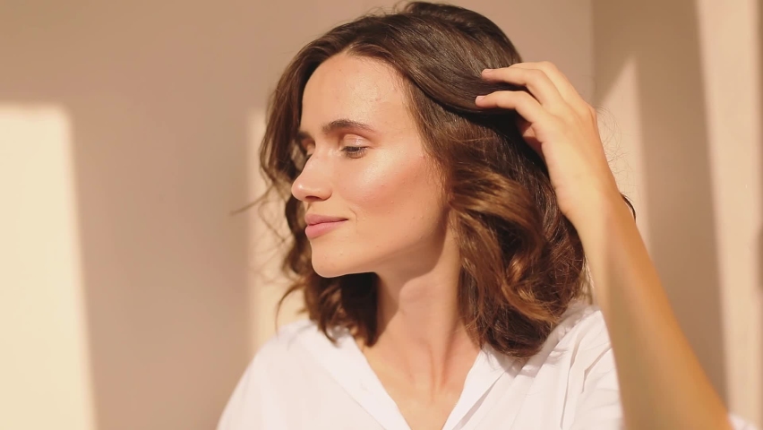 Lovely coquettish brunette woman, look playfully, flirting, fix her curly hair. Woman fix her hair at morning and next look happy. Brunette hair fashion model face smiling and look at side. | Shutterstock HD Video #1066881184