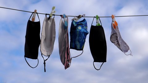 Group of reusable wet protective face masks drying outdoors on washing line against the sky during covid-19 pandemic.