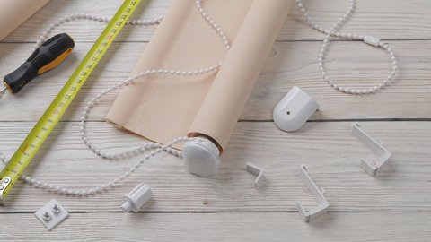 The two beige roller blinds, spare parts, mesure tape and screwdriver on a white wooden table. Preparation for the installation or repair of roller blinds.