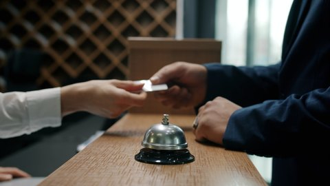 Close-up of male hands ringing call bell in hotel taking key card from receptionist while businessman is arriving and checking-in. Accommodation and people concept.