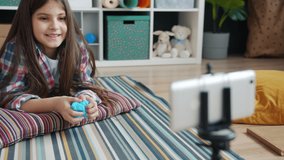 Emotional girl vlogger is recording video playing with modelling clay and speaking for smartphone camera smiling creating interesting content for children.