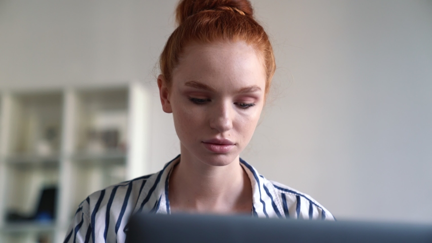 A thinking redhead woman is using her laptop computer sitting inside the apartments