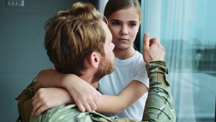 A handsome soldier man is hugging his daughter sitting at home