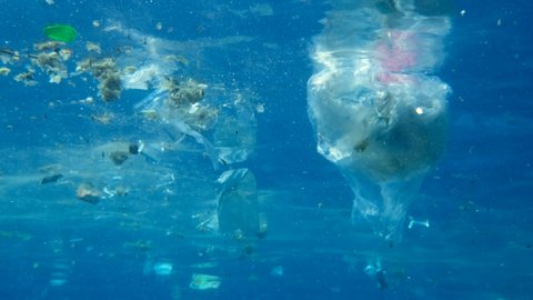 Slow motion, Massive plastic and other debris slowly drifts under surface of the blue ocean in the sunrays. Plastics garbage environmental pollution problem. Massive plastic pollution of the Ocean