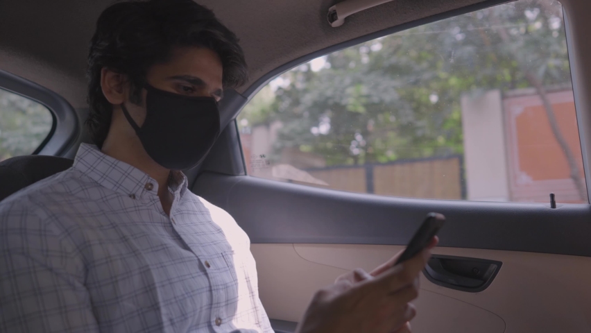 Shot of a young attractive Indian male corporate office worker sitting in a moving car to go the workplace with protective mask on his face using a mobile phone to type a text message amid COVID 19 Royalty-Free Stock Footage #1066900894