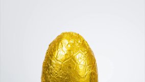 Stop motion footage of a milk chocolate Easter egg wrapped in gold foil being slowly unwrapped and eaten bite by bite until there is nothing left. White background with copy space available