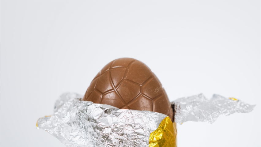 Stop motion footage of a milk chocolate Easter egg wrapped in gold foil being slowly unwrapped and eaten bite by bite until there is nothing left. White background with copy space available Royalty-Free Stock Footage #1066903771