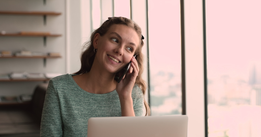 Smiling young beautiful business lady holding mobile phone call conversation with client, giving professional consultation or advice, making sales distantly while working on computer in office. Royalty-Free Stock Footage #1066905115