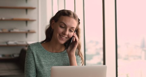Smiling young beautiful business lady holding mobile phone call conversation with client, giving professional consultation or advice, making sales distantly while working on computer in office.