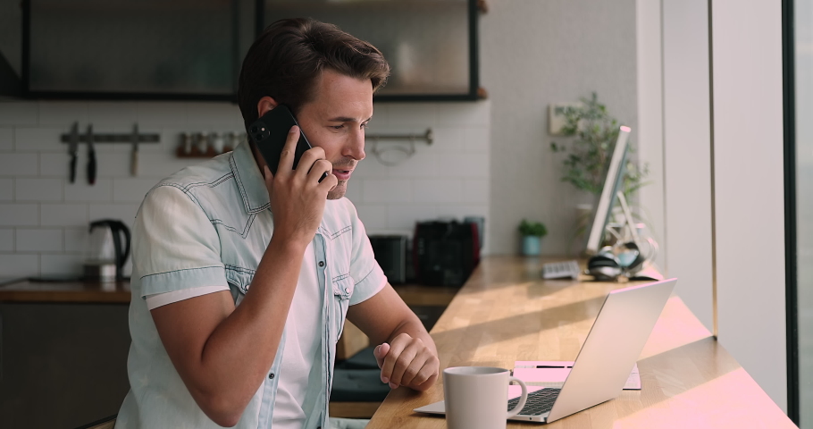 Happy young 35s man sitting at table with computer, involved in phone call conversation, confirming internet store order or communicating distantly with colleagues, telecommute multitasking concept. | Shutterstock HD Video #1066905280