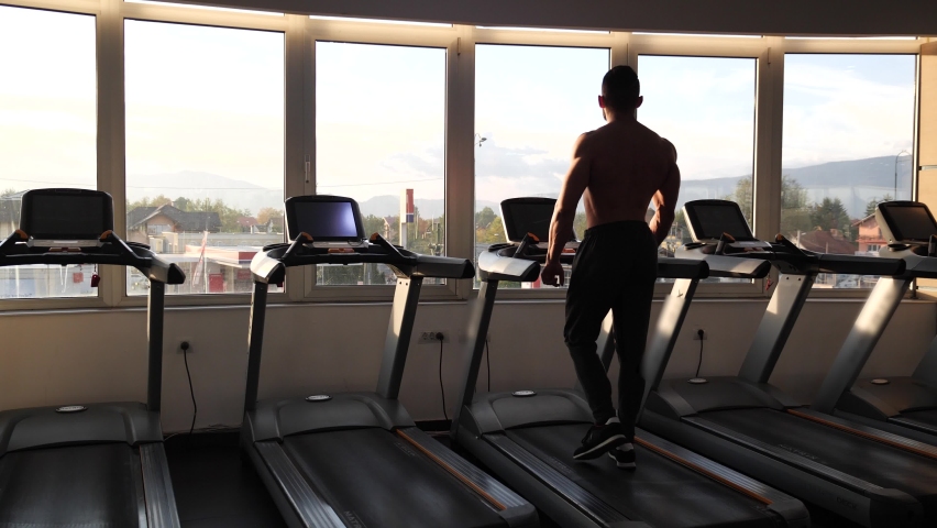 Motivated bodybuilder walking on treadmill in the early morning. Sunrise flares in front of him. | Shutterstock HD Video #1066908445