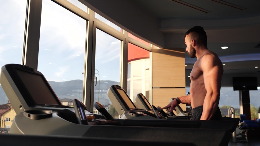 Motivated bodybuilder walking on treadmill in the early morning. Sunrise flares in front of him. | Shutterstock HD Video #1066908448