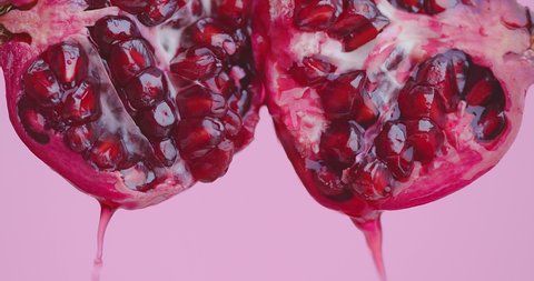 Juice drops flows down on organic red pomegranate fruit on pink studio background, fresh vitamins, close up