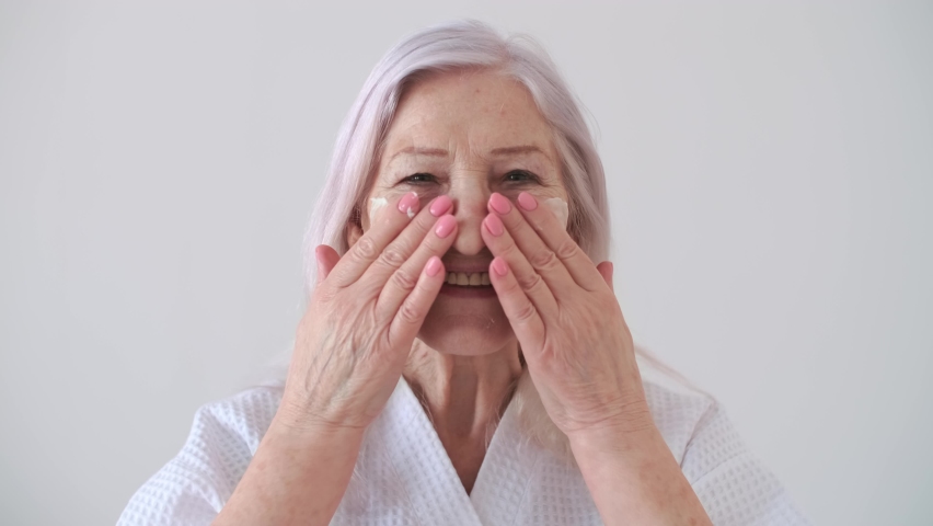 Body Love, Skin Care, Senior Woman, Home Cosmetics, Elderly Age, Cosmetic Procedures. Portrait of an elderly woman smears cream on her face and smiles | Shutterstock HD Video #1066910227