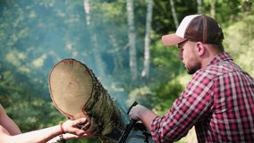 A woodcutter or logger saws firewood with a chainsaw in the forest. The woodcutter's assistant holds the sawn-off part of the tree. Favorite work at sunny day in the forest. High quality 4K video