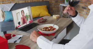 Diverse couple on a valentines date video call using laptop eating and drinking wine woman on laptop screen. online valentines day during quarantine lockdown.