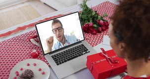Diverse couple on a valentines date video call man on screen talking to woman opening gift. online valentines day during quarantine lockdown.