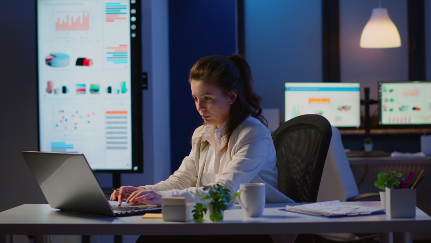 Business woman working overtime checking team project, taking notes, drinking coffee, analysing financial documents sitting at desk in startup company late at night using modern technology network | Shutterstock HD Video #1066924657